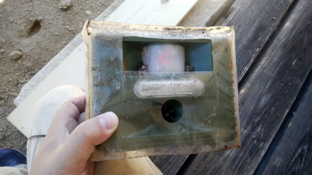 【長野県の施工実績】安曇野市穂高|木造住宅の妻飾り通気から天井裏へ侵入していたコウモリを防除した事例 2 長野県安曇野市のコウモリ駆除現場で回収された、ホームセンターで購入された市販の動物忌避用超音波機器。コウモリに対する効果がなく、機器のセンサー部分や内部にまでコウモリの糞が入り込み、汚染されている様子。